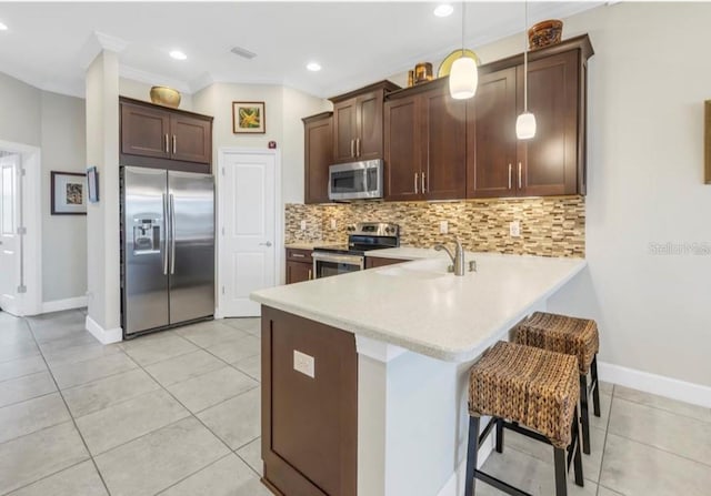 kitchen with a breakfast bar, decorative light fixtures, stainless steel appliances, light countertops, and a sink