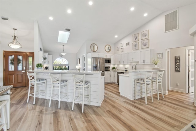 kitchen featuring appliances with stainless steel finishes, pendant lighting, white cabinetry, a breakfast bar area, and light hardwood / wood-style flooring