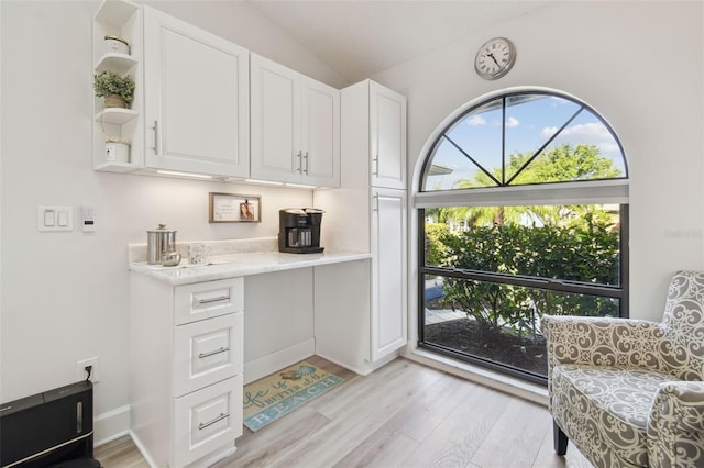 interior space with light stone counters, vaulted ceiling, light hardwood / wood-style flooring, and white cabinets