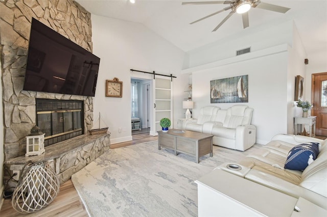 living room with a barn door, high vaulted ceiling, light wood-type flooring, ceiling fan, and a fireplace