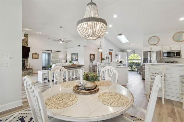 dining room with a skylight, high vaulted ceiling, light hardwood / wood-style flooring, ceiling fan, and a barn door