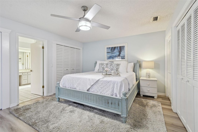 bedroom featuring ensuite bath, light hardwood / wood-style flooring, ceiling fan, a textured ceiling, and multiple closets