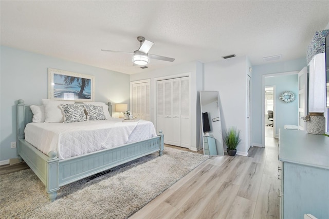 bedroom featuring ceiling fan, a textured ceiling, light hardwood / wood-style floors, and multiple closets