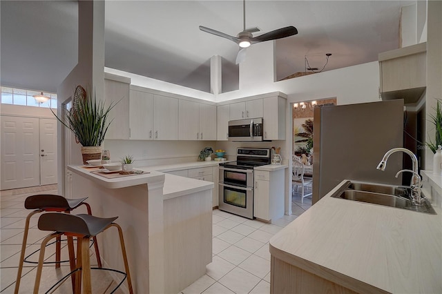 kitchen featuring a breakfast bar, sink, light tile patterned floors, kitchen peninsula, and stainless steel appliances