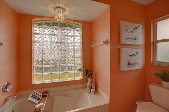 bathroom with a healthy amount of sunlight, a tub to relax in, and toilet