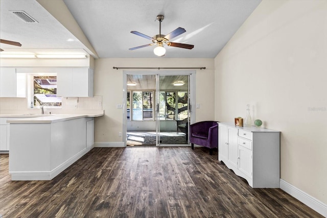 interior space with dark wood-type flooring, lofted ceiling, kitchen peninsula, white cabinets, and backsplash