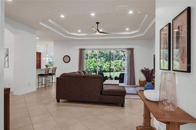 living room featuring light tile patterned floors, ceiling fan, and a tray ceiling