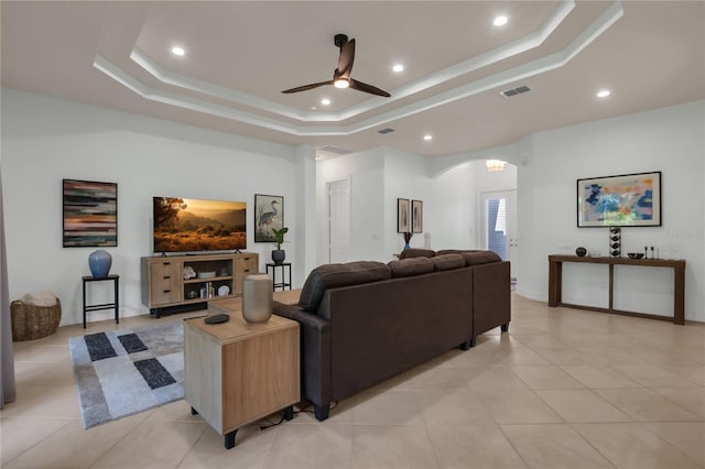 living room featuring light tile patterned flooring, ceiling fan, and a tray ceiling