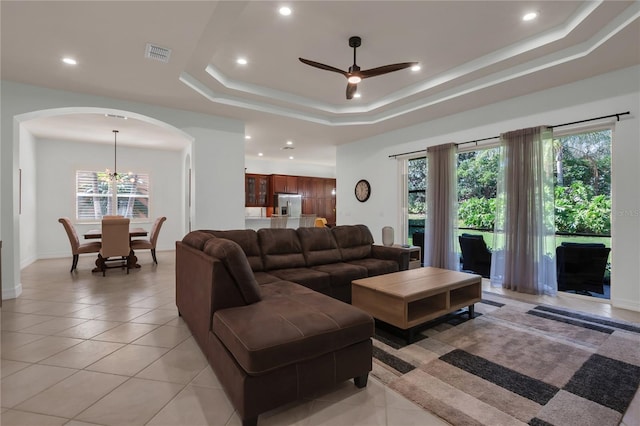tiled living room featuring a healthy amount of sunlight, ceiling fan with notable chandelier, and a tray ceiling