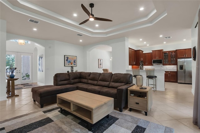 living room with light tile patterned flooring, ceiling fan, and a tray ceiling
