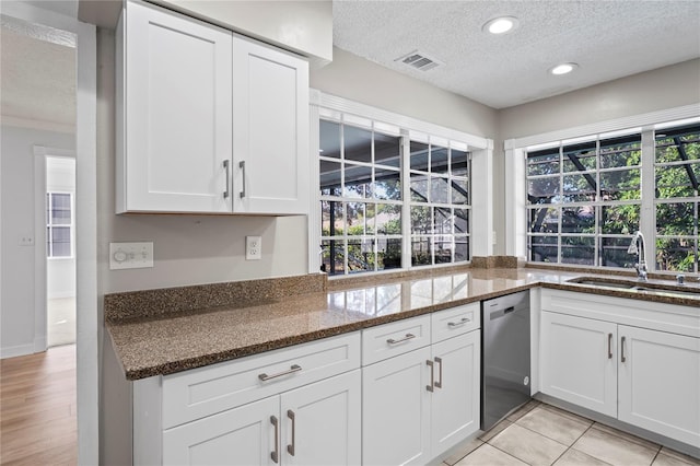 kitchen featuring sink, a textured ceiling, dark stone countertops, stainless steel dishwasher, and white cabinets