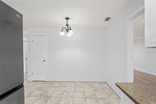 unfurnished dining area featuring a notable chandelier, light tile patterned floors, and a textured ceiling