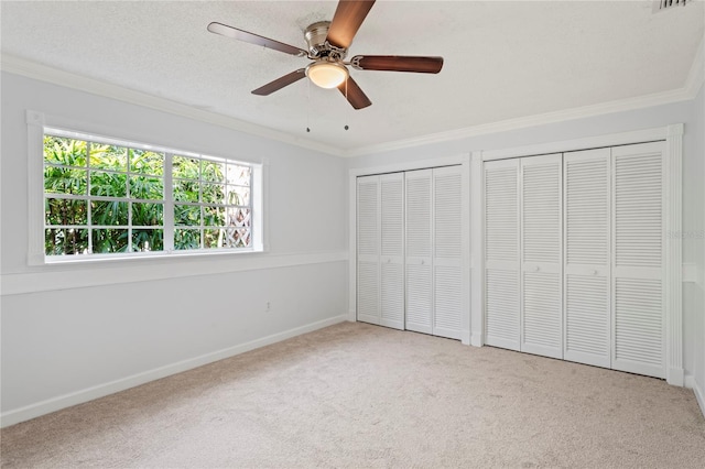 unfurnished bedroom with multiple closets, crown molding, light carpet, and a textured ceiling