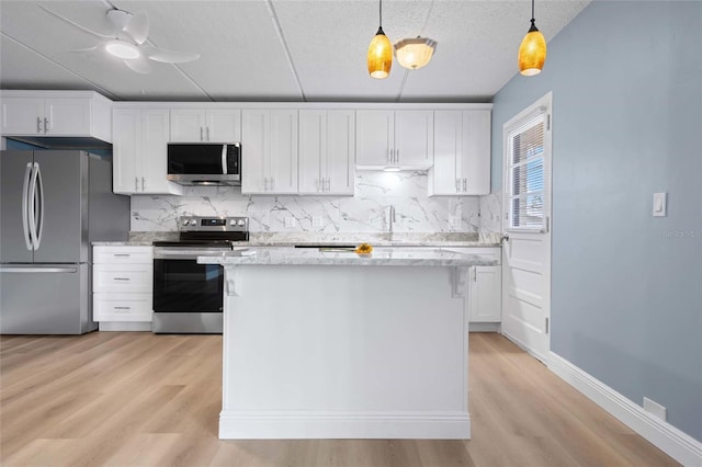 kitchen featuring pendant lighting, white cabinetry, stainless steel appliances, a center island, and light stone counters