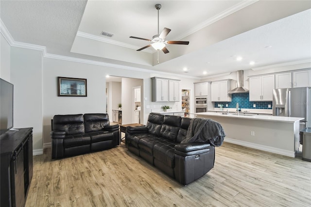 living area with crown molding, a tray ceiling, visible vents, and light wood-style floors