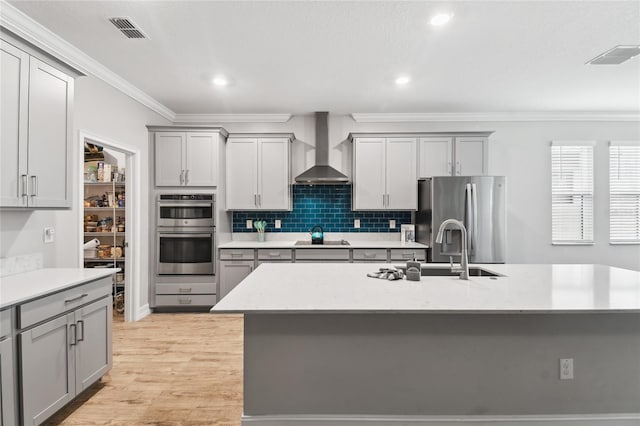 kitchen with gray cabinetry, stainless steel appliances, visible vents, ornamental molding, and wall chimney range hood