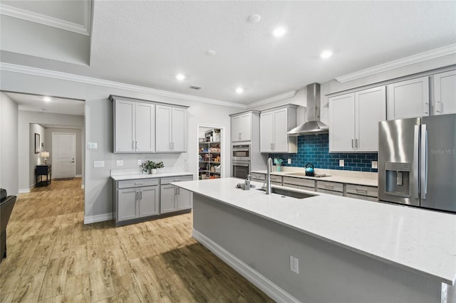 kitchen with gray cabinetry, appliances with stainless steel finishes, light wood-style floors, a sink, and wall chimney range hood