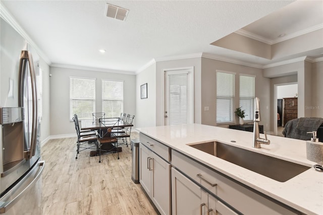 kitchen featuring light stone counters, light wood-style flooring, a sink, visible vents, and freestanding refrigerator