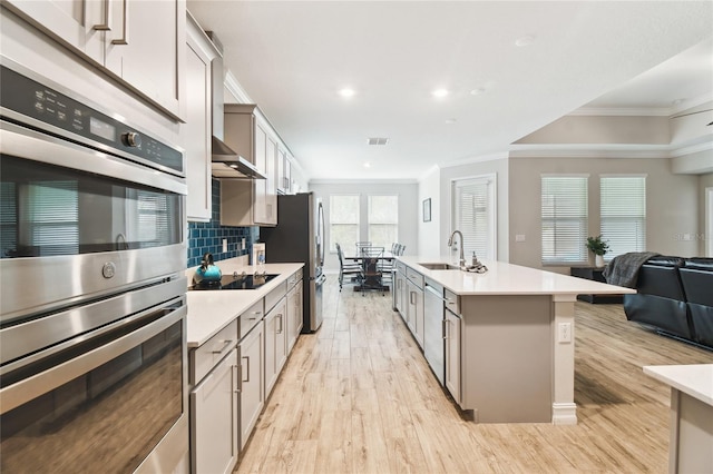 kitchen featuring crown molding, tasteful backsplash, light wood-style flooring, appliances with stainless steel finishes, and open floor plan