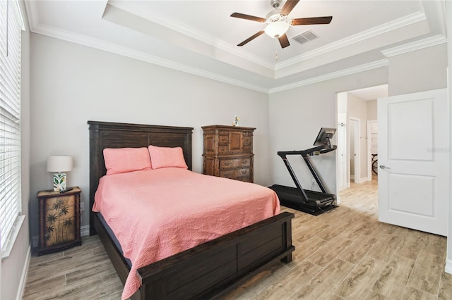 bedroom with ornamental molding, light wood-type flooring, a raised ceiling, and visible vents