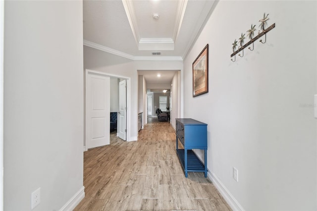 corridor featuring visible vents, baseboards, a tray ceiling, crown molding, and light wood-type flooring