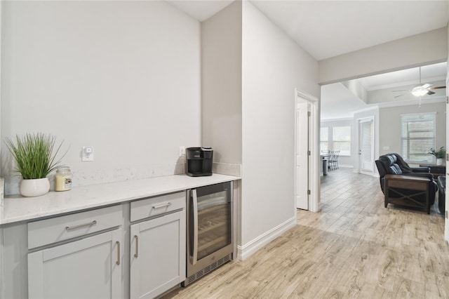 bar featuring ornamental molding, ceiling fan, light wood-type flooring, beverage cooler, and baseboards