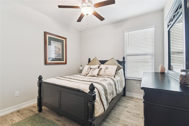 bedroom featuring baseboards, ceiling fan, light wood finished floors, and multiple windows