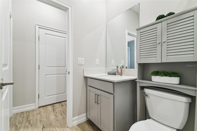 bathroom with toilet, baseboards, wood finished floors, and vanity