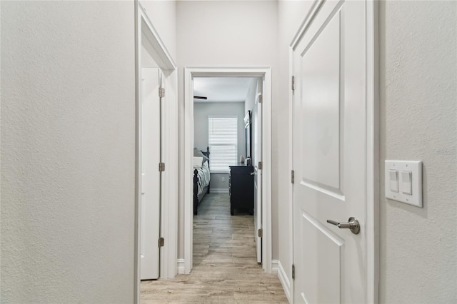 corridor with light wood-type flooring, baseboards, and a textured wall