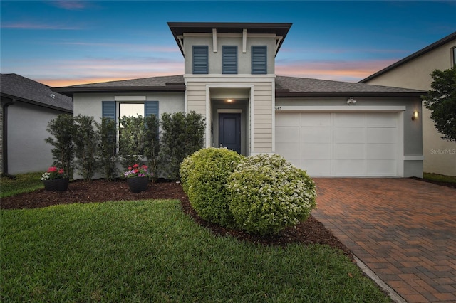 view of front of property with decorative driveway, roof with shingles, stucco siding, a front yard, and a garage