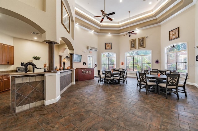 kitchen featuring an AC wall unit, decorative columns, ceiling fan, a raised ceiling, and crown molding