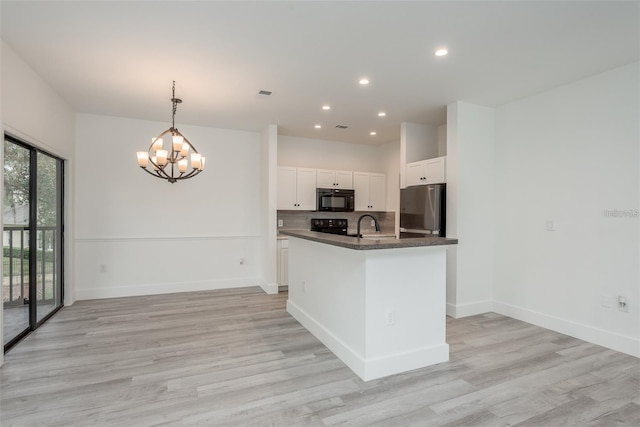 kitchen with decorative light fixtures, tasteful backsplash, white cabinetry, black appliances, and a center island with sink