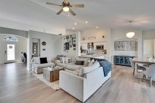 living room with lofted ceiling, ceiling fan with notable chandelier, and light hardwood / wood-style flooring