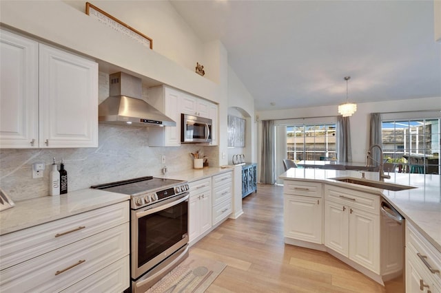 kitchen with pendant lighting, white cabinetry, sink, stainless steel appliances, and wall chimney exhaust hood