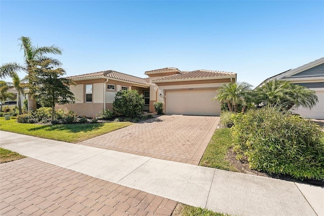 mediterranean / spanish home featuring stucco siding, decorative driveway, a front yard, a garage, and a tiled roof