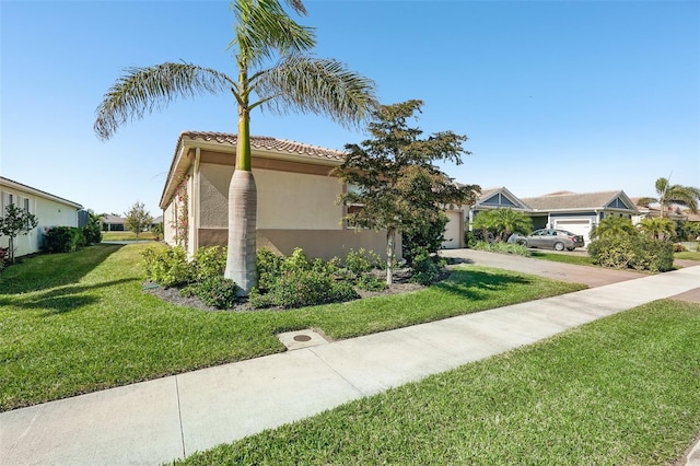 view of side of property featuring stucco siding, a yard, concrete driveway, an attached garage, and a tiled roof