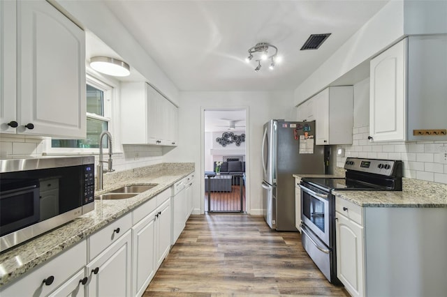 kitchen with sink, white cabinets, backsplash, stainless steel appliances, and light wood-type flooring