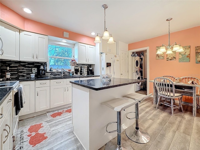 kitchen with pendant lighting, stacked washer and dryer, white refrigerator with ice dispenser, and white cabinets