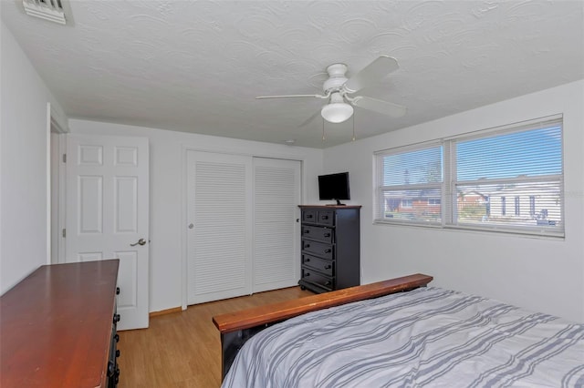 bedroom featuring a textured ceiling, light hardwood / wood-style flooring, a closet, and ceiling fan