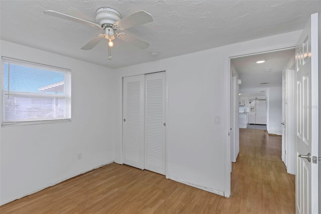 unfurnished bedroom featuring white refrigerator with ice dispenser, a textured ceiling, a closet, and light wood-type flooring