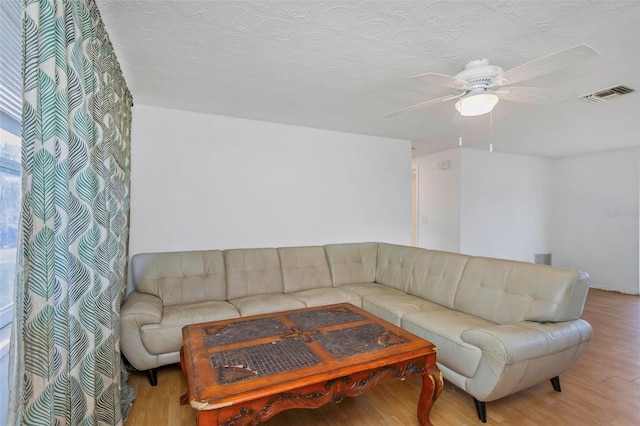 living room with a textured ceiling, ceiling fan, and light hardwood / wood-style flooring