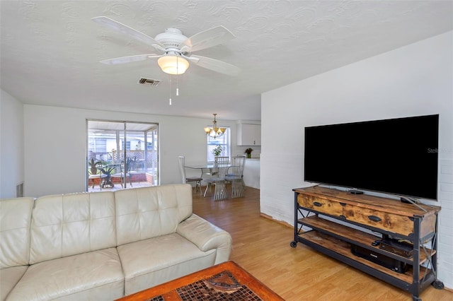 living room featuring ceiling fan with notable chandelier, a textured ceiling, and light wood-type flooring