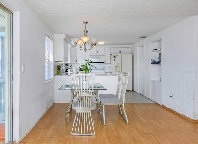 dining area with built in shelves, light hardwood / wood-style floors, a textured ceiling, and a notable chandelier