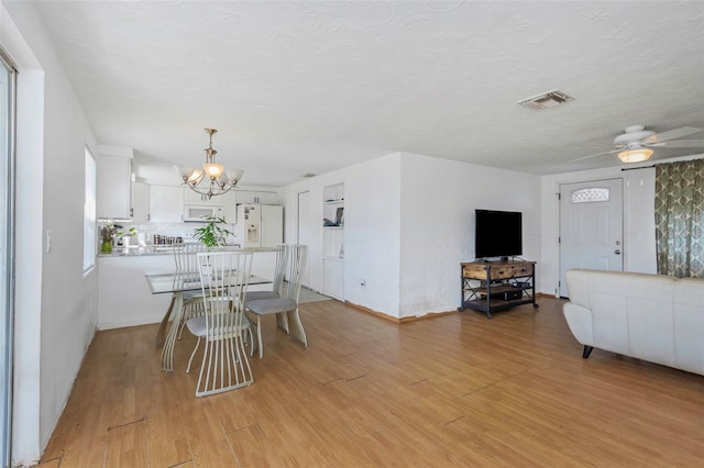 dining area featuring ceiling fan with notable chandelier, a textured ceiling, and light wood-type flooring