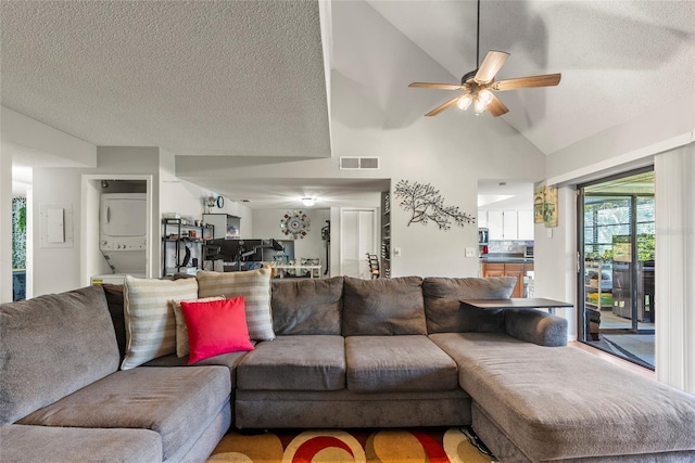 living room featuring ceiling fan, stacked washer and clothes dryer, lofted ceiling, and a textured ceiling