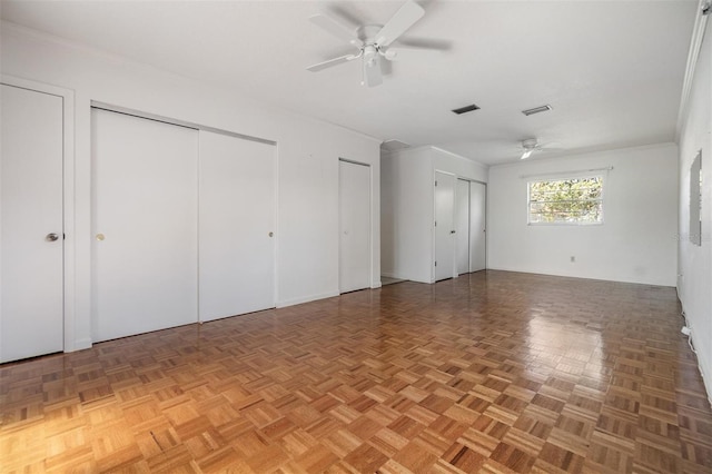 unfurnished bedroom featuring parquet floors, ceiling fan, crown molding, and two closets