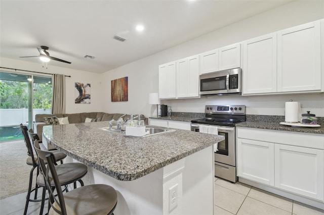 kitchen with stainless steel appliances, a kitchen breakfast bar, light tile patterned floors, a ceiling fan, and dark stone counters