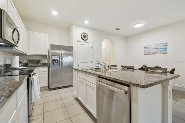 kitchen featuring stainless steel appliances, a sink, light tile patterned floors, arched walkways, and a kitchen island with sink