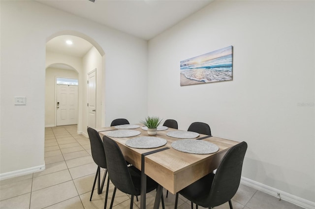 dining space with light tile patterned flooring, arched walkways, and baseboards