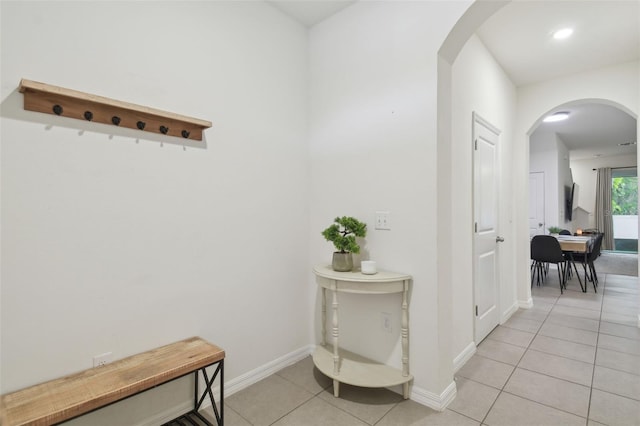 hall featuring light tile patterned flooring, arched walkways, baseboards, and recessed lighting